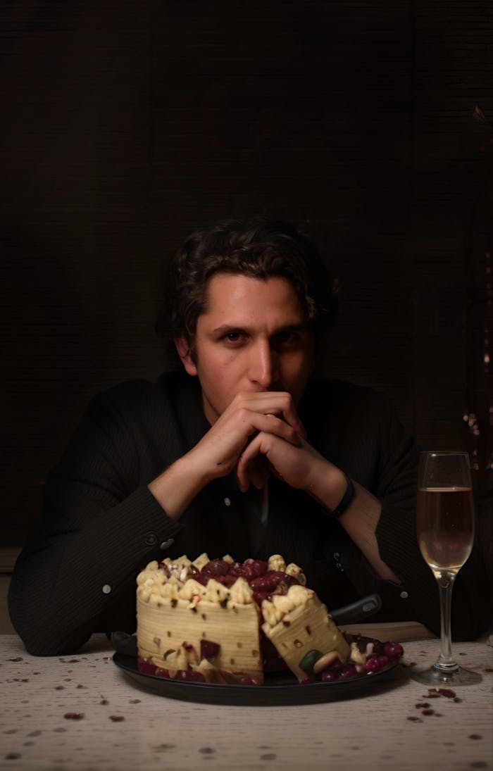 Moody portrait of a man with cake and champagne, capturing mystery and contemplation.