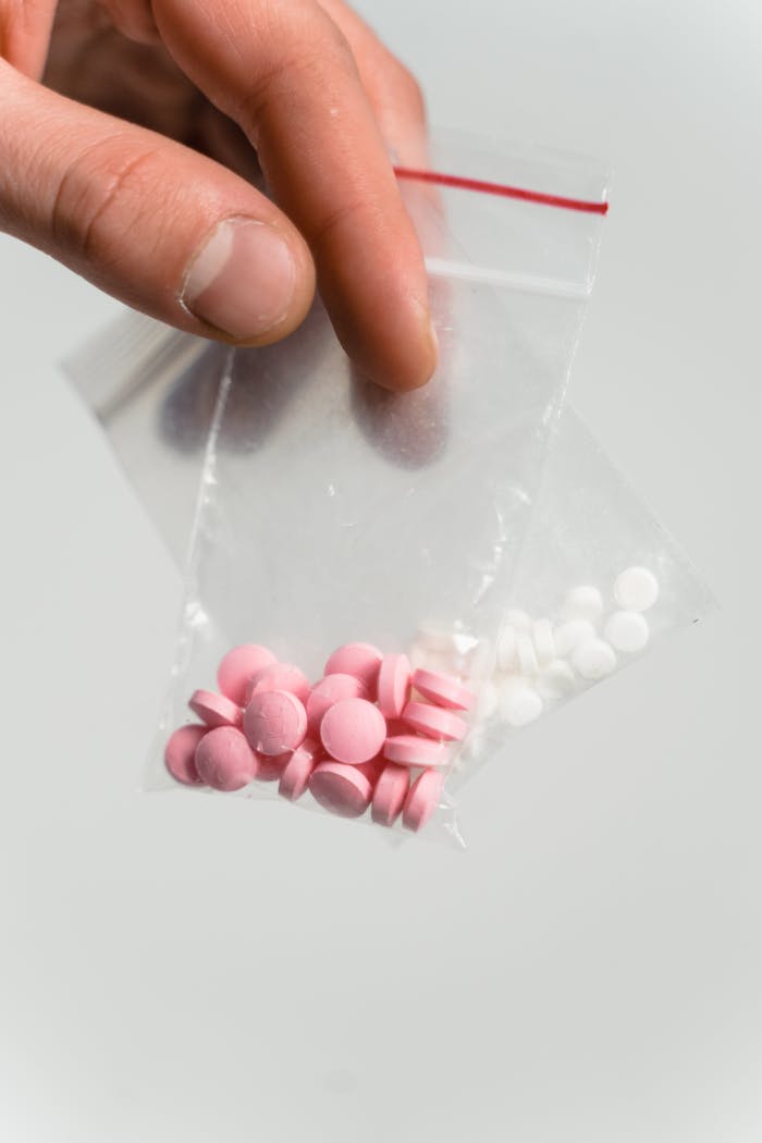 hero-img Hand holding a ziplock bag with pink and white pills on a white background.